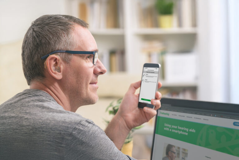 Adult male setting up his hearing aids with his smartphone.